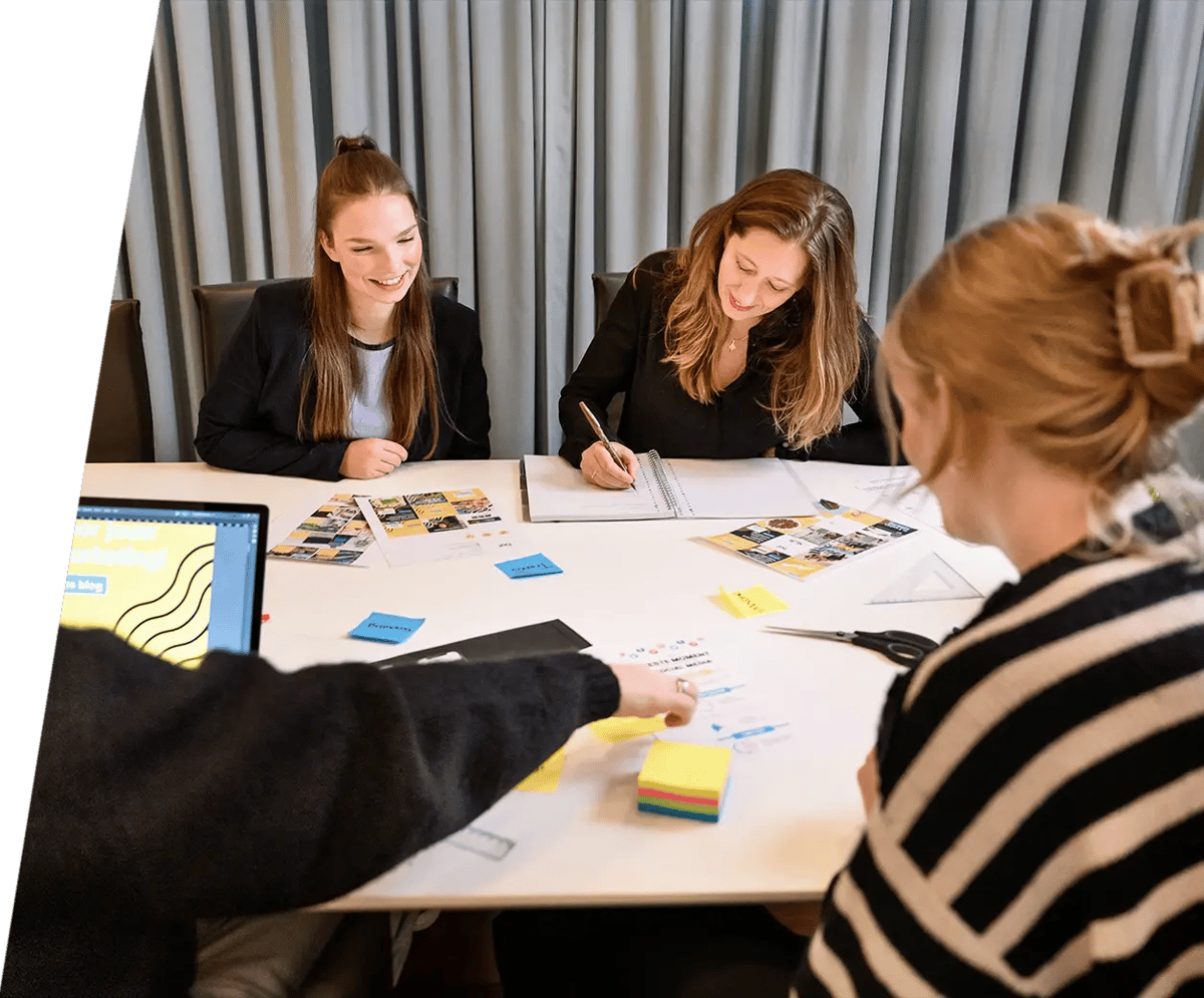 Collega's werken samen rond een tafel vol notities en post-its, terwijl ze ideeën uitwisselen om tot het beste resultaat te komen